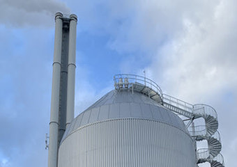 toppen av akkumulatortank. tanken er rund og belagt med stålplater, det går en spiraltrapp opp til toppen. I bakgrunn vises pipe tilhørende forbrenningsanlegget på Tiller